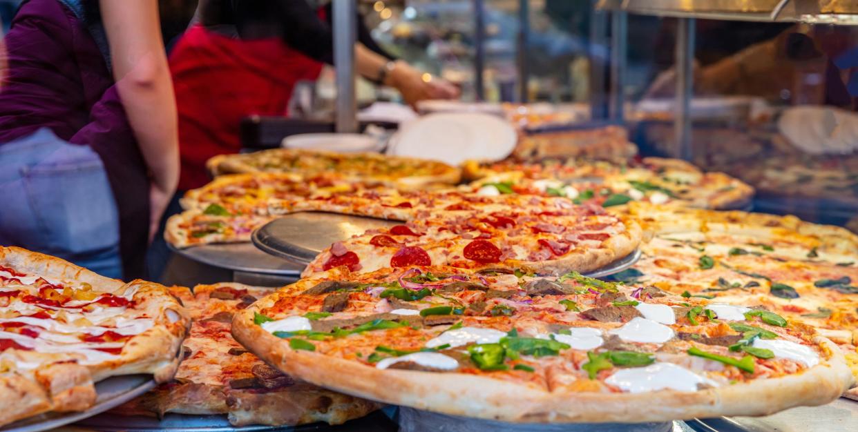 Pizzeria glass window. Variety of italian pizzas in a shop display, street food. Kitchen workers arranging the pizzas.