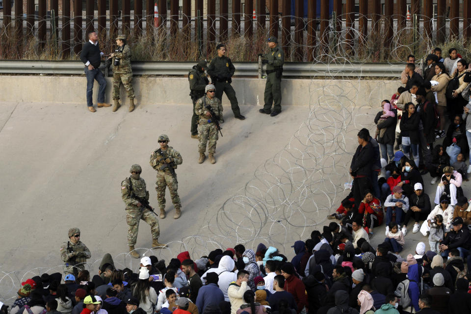 FILE - Migrants congregate on the banks of the Rio Grande at the U.S. border with Mexico, Dec. 20, 2022, where members of the Texas National Guard cordoned off a gap in the U.S. border wall. The Biden administration has stopped taking appointments via its mobile phone app from asylum seekers in a notoriously dangerous and corrupt Mexican border city amid signs migrants who used it were being targeted for extortion.(AP Photo/Morgan Lee, File)