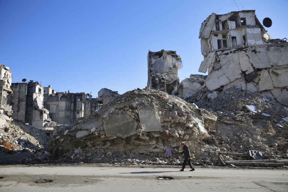 FILE - In this Jan. 20, 2018 file photo, a Syrian man walks through the destruction of the Salaheddine neighborhood in the eastern Aleppo, Syria. In Syria nowadays, there is an impending fear that all doors are closing. After nearly a decade of war, the country is crumbling under the weight of years-long western sanctions, government corruption and infighting, a pandemic and an economic downslide made worse by the financial crisis in Lebanon, Syria's main link with the outside world. (AP Photo/Hassan Ammar, File)