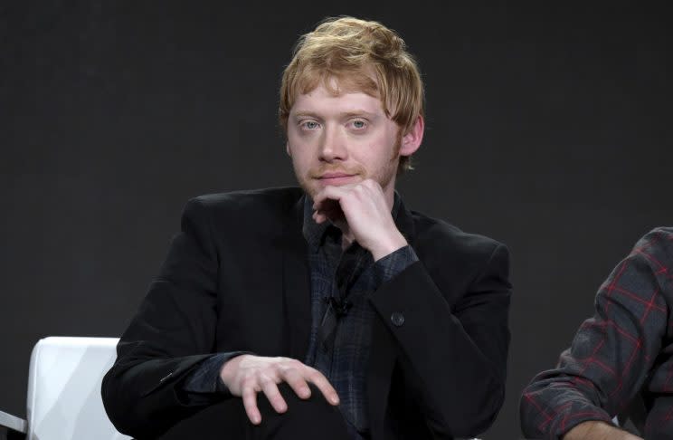 Rupert Grint sits onstage in black.