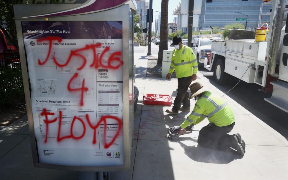 Workers remove graffiti from the sidewalk at a bus stop in Phoenix in the aftermath of a demonstration  - AP