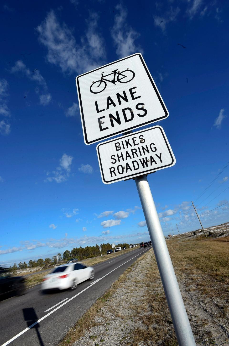 Eastbound motorists traveling U.S. Highway 98 on Okaloosa Island Tuesday pass signs that say share the road with bicyclists. Gov. Ron DeSantis signed legislation last year that states no-passing zones do not apply to drivers who safely and briefly drive to the left of center of the road to pass a bicycle or pedestrian.