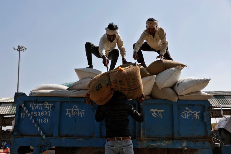 Laborers unload sacks filled with wheat at a wholesale grain market in Mathura