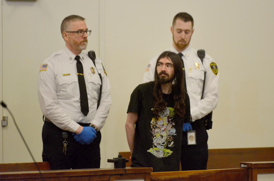 Justin Moreira, center, looks out into the audience from the prisoner dock during his arraignment March 7 in Barnstable District Court. A Barnstable County grand jury has indicted Moreira on 49 counts, including armed assault to murder, kidnapping and weapons charges. He has pleaded not guilty to those charges.
