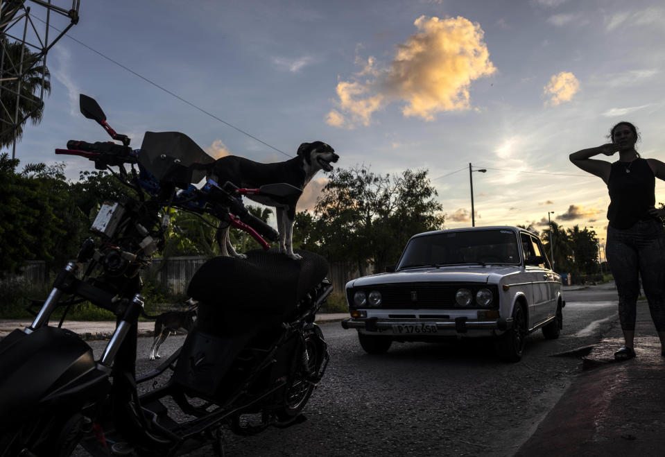 Kiara stands on an electric scooter as people work on their electric scooters after attending a gathering in the capital of stunts and races, outside her caretaker's home in Cojimar, Cuba, Friday, July 15, 2022. Cuba has been flooded in recent years with “motorinas”, as these electric scooters are called on the island, a fad for many, but also a solution to the transportation problems and fuel shortages that overwhelm the Caribbean nation. (AP Photo/Ramon Espinosa)