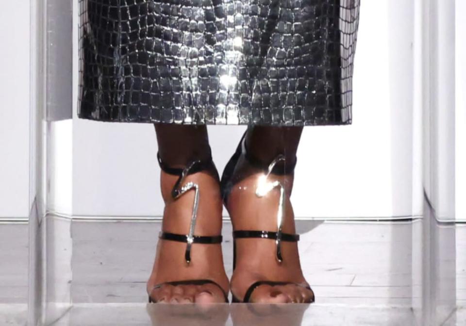 A closer look at Haddish wearing strappy black patent leather Giuseppe Zanotti sandals featuring a decorative silver metal G-logo accessory with sparkling rhinestones. - Credit: Randy Shropshire