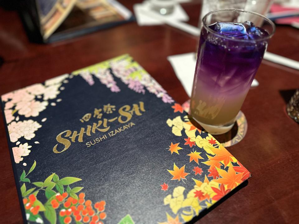 menu for shiki sai next to a colorful cocktail on the table at the epcot restaurant