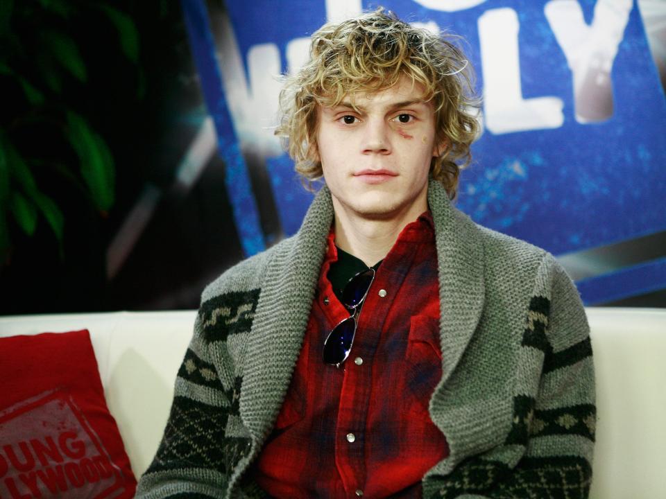 Evan Peters in 2011 wearing a sweater and sitting on a couch