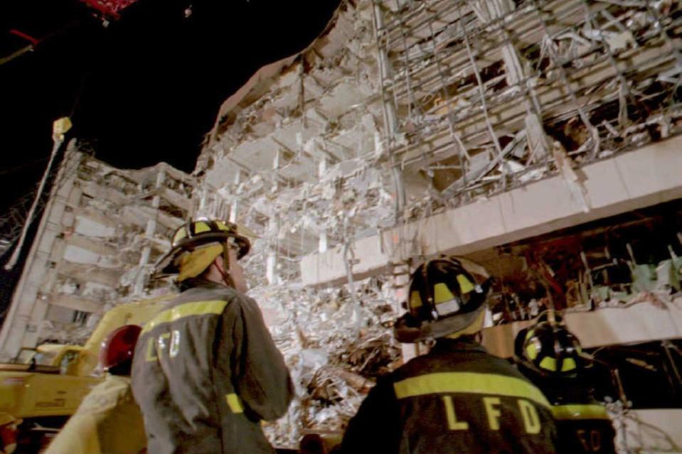 two firefighters stand and look up at a nine story building that has been destroyed and remains partially exposed