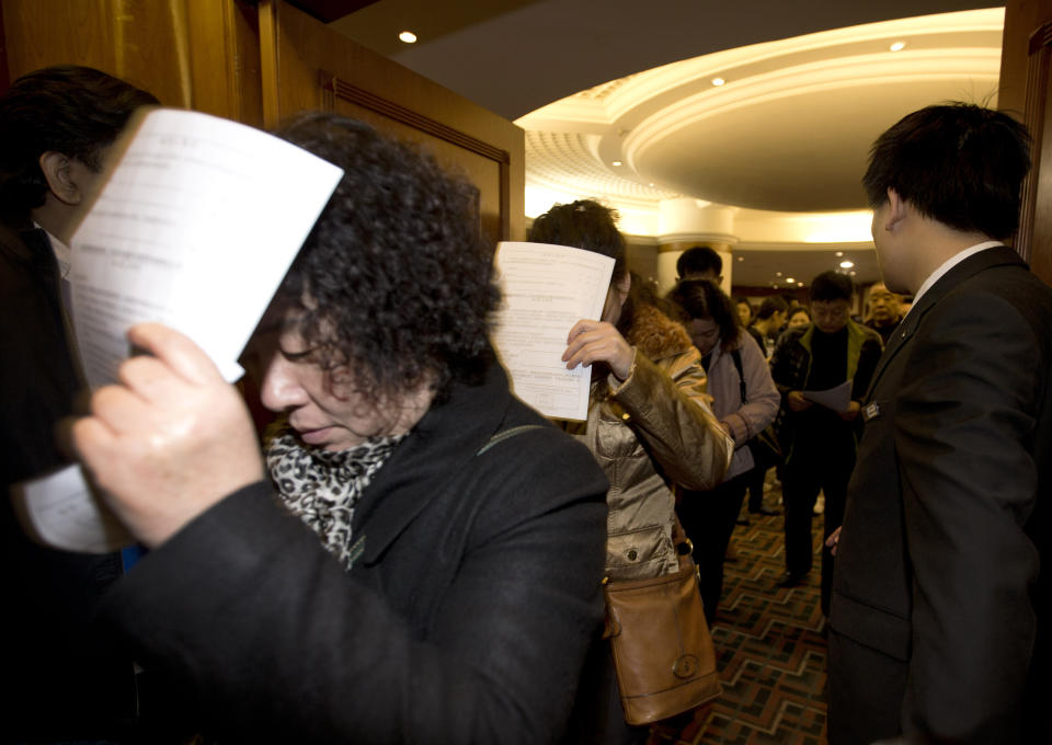 Chinese relatives of passengers aboard a missing Malaysia Airlines plane use application documents to block their faces as they walk out of a hotel room in Beijing Monday, March 10, 2014. The anguished hours had turned into a day and a half. Fed up with awaiting word on the missing plane, relatives of passengers in Beijing lashed out at the carrier with a handwritten ultimatum and an impromptu news conference. (AP Photo/Andy Wong)