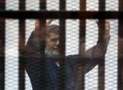 Deposed President Mursi greets his lawyers and people from behind bars after his verdict at a court on the outskirts of Cairo