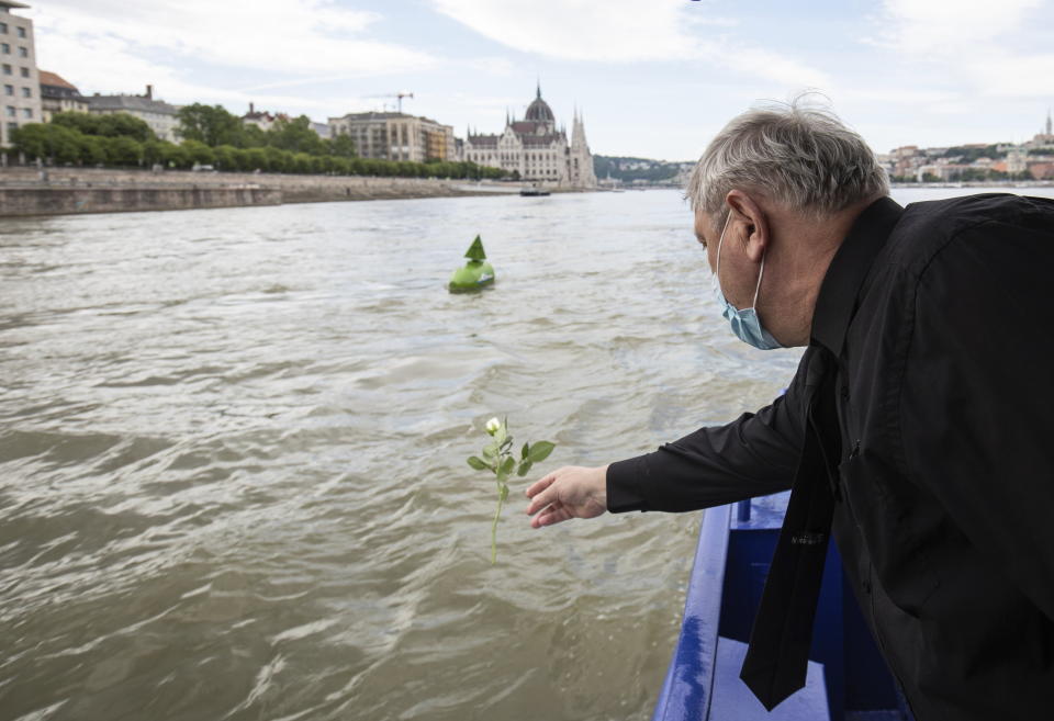 A man throws a flower into River Danube from a ship during an ecumenical commemoration marking the second anniversary of a fatal boat accident on the River Danube , in Budapest, Hungary, Saturday, May 29, 2021. Over two dozen South Korean tourists died after their tour boat collided with a river cruise ship on the Danube River. (Balazs Mohai/MTI via AP)