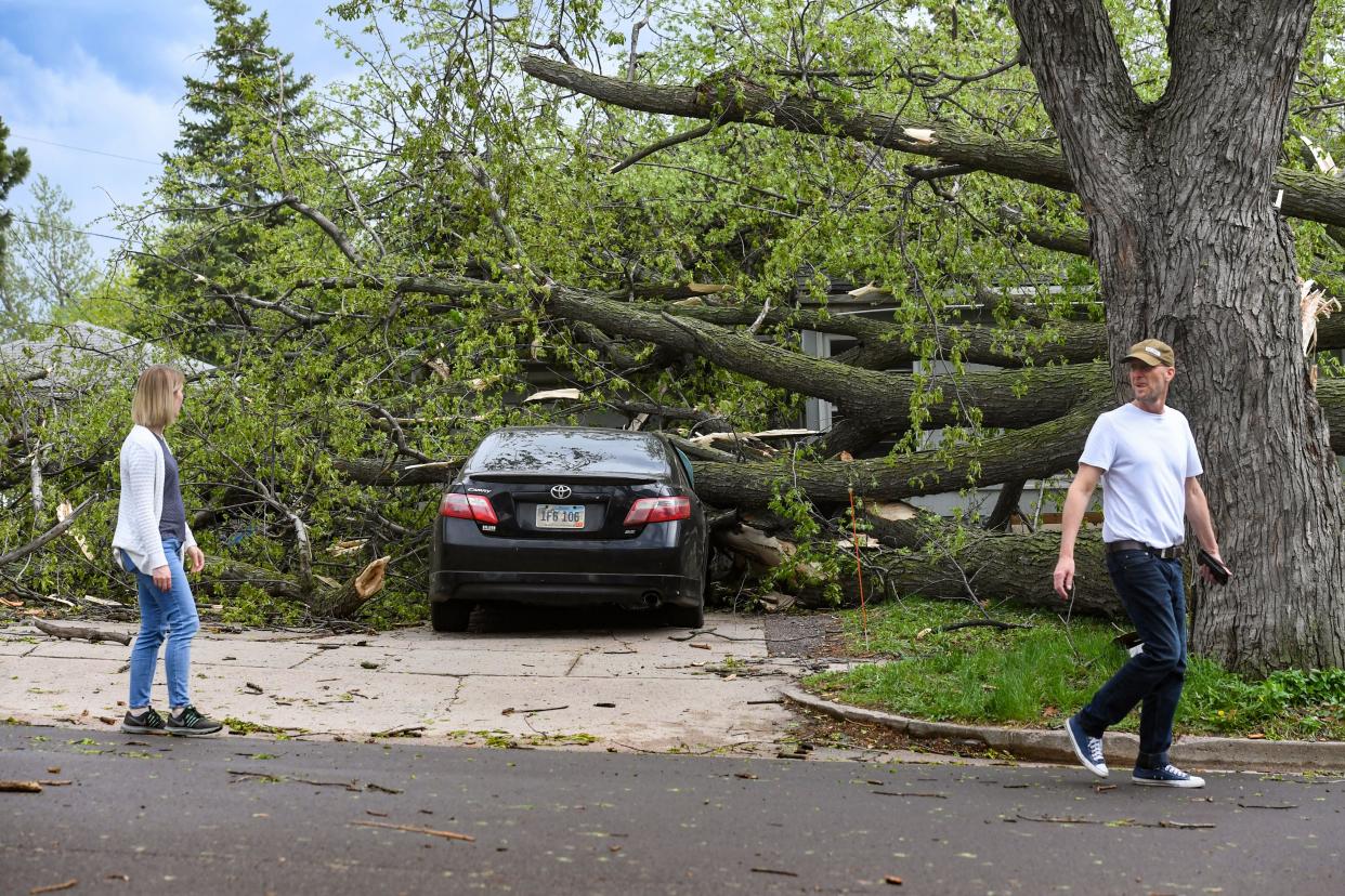 Neighbors walk past a car crushed by tree limbs on 36th Street on Thursday, May 12, 2022, in Sioux Falls.