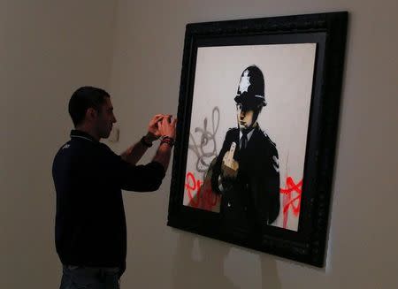 A man takes a picture of an artwork by British street artist known as Banksy during the exhibition "War, Capitalism & LIiberty" organized by "Fondazione Terzo Pilastro" in Rome, Italy May 23, 2016. REUTERS/Tony Gentile