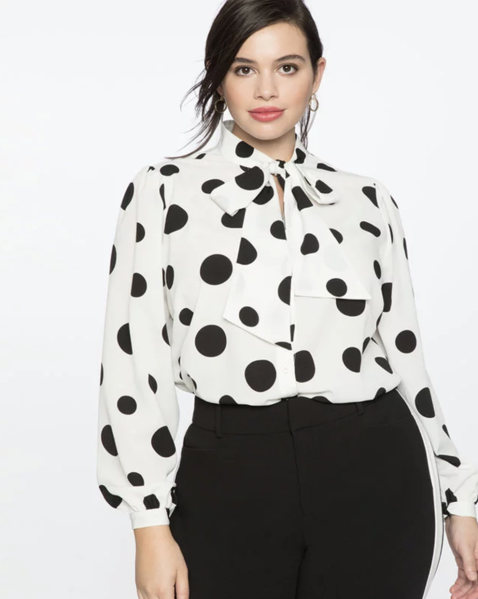 plus size model in black pants and white and black polka dot Tie Neck Blouse (Photo via Eloquii)