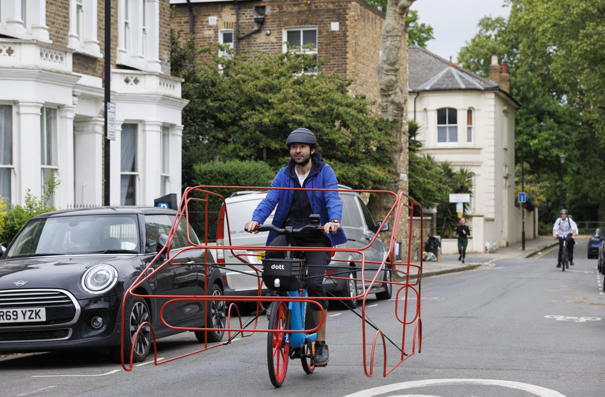 A cyclist wearing a frame in the shape of a car in west London (Dott/PA)