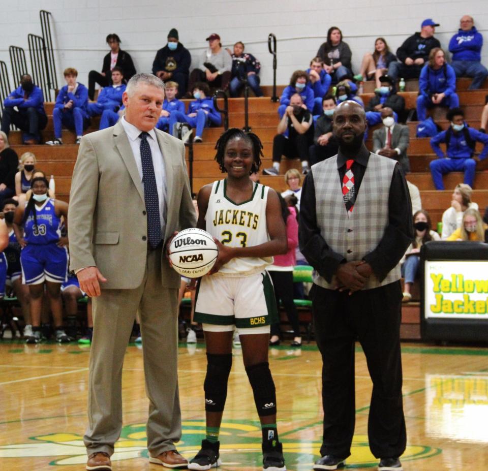 With Bessemer City girls basketball coach Billy James and assistant Danny McDowell, junior standout Janiya Adams accepts a basketball commemorating her 1,000th career point on Jan. 7, 2021.