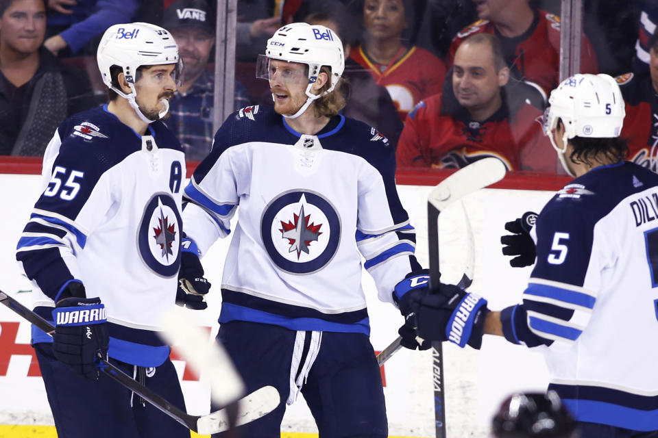 Winnipeg Jets' Kyle Connor, center, celebrates his goal against the Calgary Flames with Mark Scheifele, left, and Brenden Dillon during the third period of an NHL hockey game Saturday, Nov. 27, 2021, in Calgary, Alberta. (Larry MacDougal/The Canadian Press via AP)