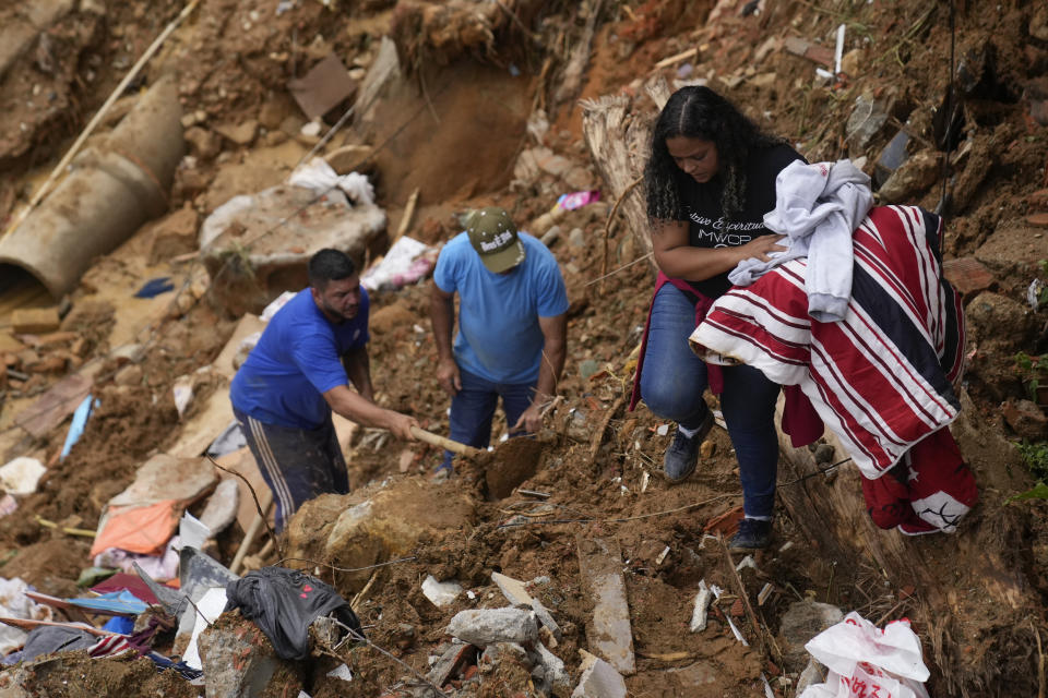 Priscilla Neves recovers belongings while waiting for news about her missing parents, who were in their family home when it was covered by mudslides, in Petropolis, Brazil, Wednesday, Feb. 16, 2022. Neves was not in the home when extremely heavy rains set off mudslides and floods in a mountainous region of Rio de Janeiro state, killing multiple people. (AP Photo/Silvia Izquierdo)