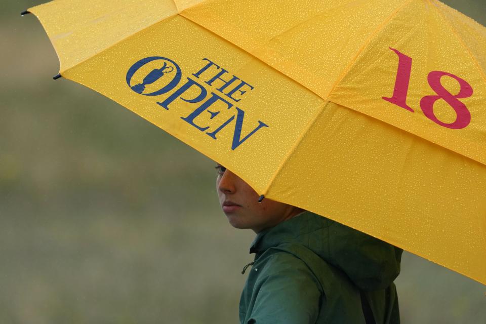 Jul 22, 2023; Hoylake, ENGLAND, GBR; A spectator watches under an umbrella as rain falls during the third round of The Open Championship golf tournament at Royal Liverpool.