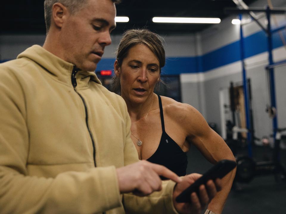 Coach Ben Bergeron in a gym working with an athlete, looking at a fitness app on a phone