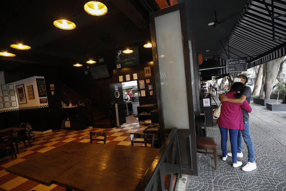 A young couple hug as they wait for their takeout lunch order, outside Argentine steakhouse Quebracho in the Cuauhtemoc neighborhood of Mexico City, Sunday, Jan. 10, 2021. Quebracho is one of many restaurants in the capital and adjacent Mexico State which are banning together in a campaign dubbed "Abrir o Morir," Spanish for "Open or Die," and plan to open their doors to diners again on Monday in defiance of ordinances limiting restaurants to takeout service while the Mexico Valley remains under a COVID-19 pandemic red alert. (AP Photo/Rebecca Blackwell)