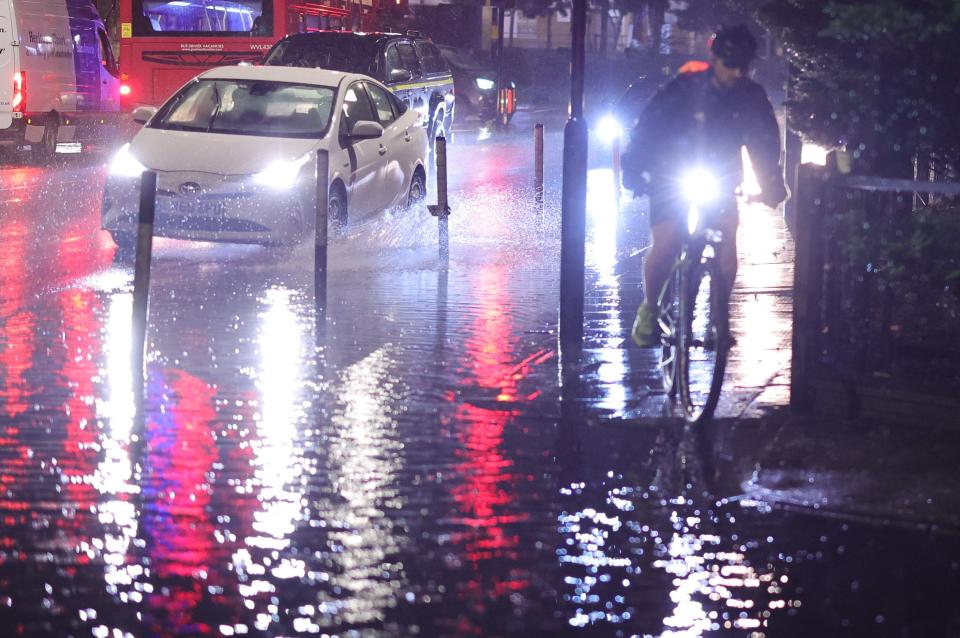 Cyclists attempt to navigate a section of partially flooded road in Colliers Wood (George Cracknell Wright)