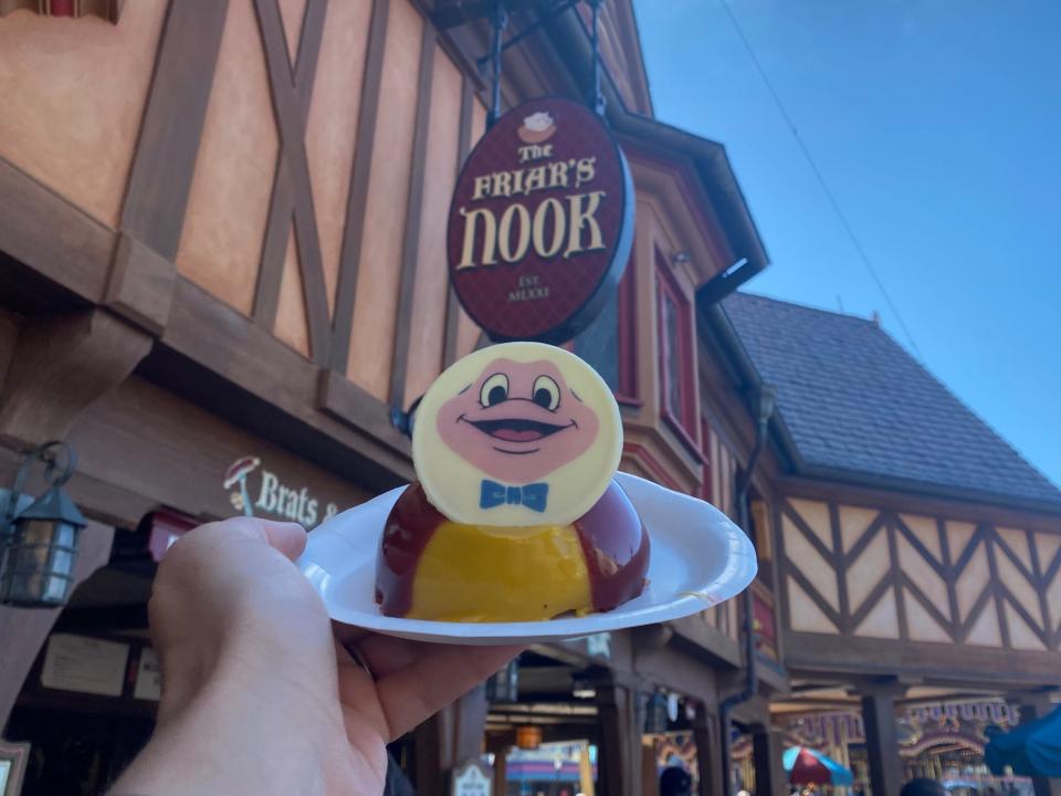 hand holding mr toad dome cake in front of friars nook magic kingdom