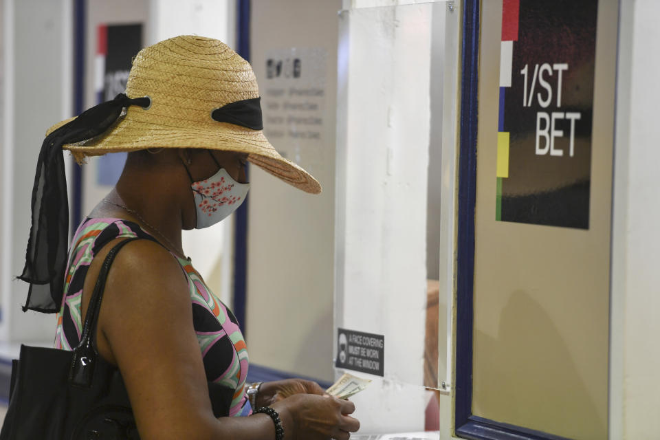 A woman wears a face mask to protect against the spread of COVID-19 and a hat while placing a bet ahead of the Preakness Stakes horse race at Pimlico Race Course, Saturday, May 15, 2021, in Baltimore. (AP Photo/Will Newton)