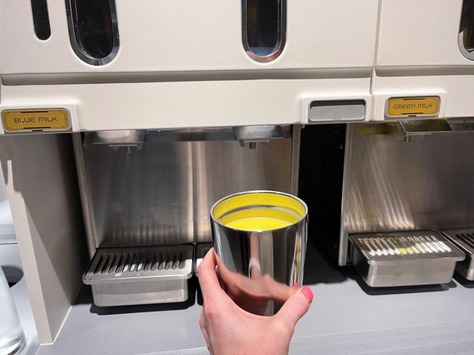 The green milk and blue milk dispensers on the Starcruiser with the writer holding a cup in front of one