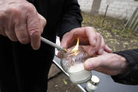 A man helps a person to light a candle to place at a new memorial paying tribute to some 60 Jews executed in the town during the Holocaust in Wojslawice, Poland, on Thursday Oct. 14, 2021. It is one of many mass grave sites to be discovered in recent years in Poland, which during World War II was occupied by Adolf Hitler’s forces. (AP Photo/Czarek Sokolowski)