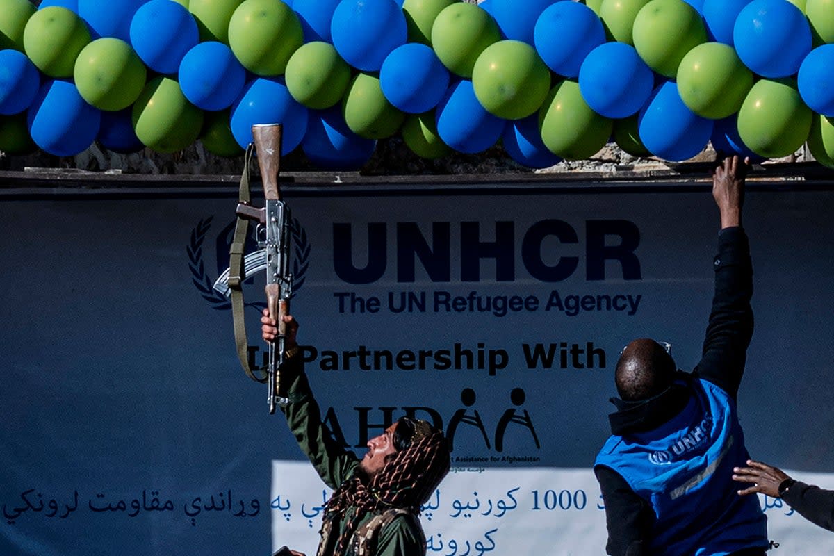 A member of Taliban security adjust balloons with his gun during a handover ceremony of newly built houses constructed by the United Nations refugee agency (UNHCR) in Paktika province (AFP via Getty Images)