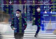 Passersby wearing protective face masks are reflected on a screen displaying stock prices outside a brokerage in Tokyo