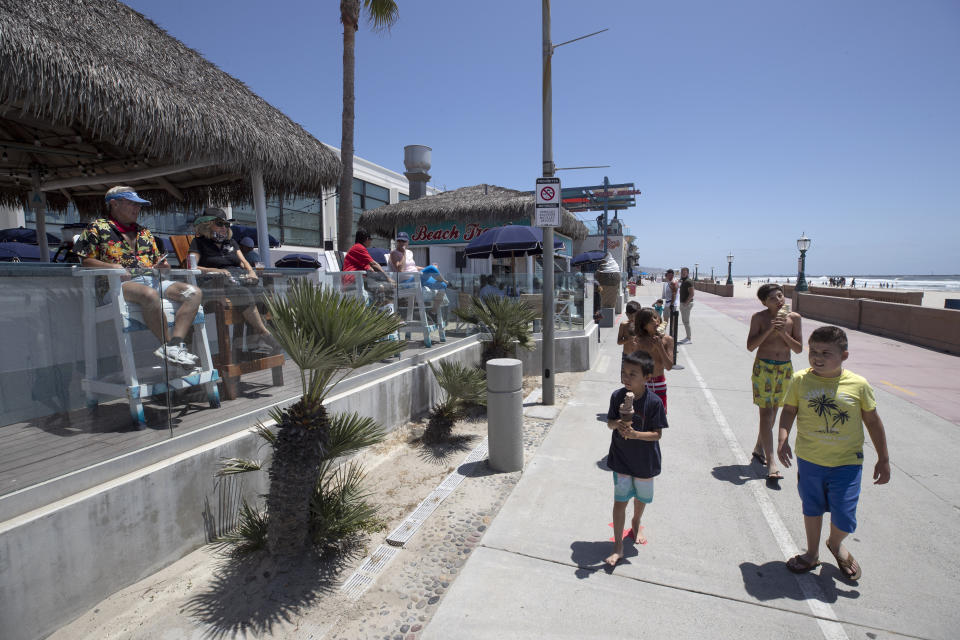 People sit at a beachfront restaurant, left, as children carrying ice cream pass, Friday, May 22, 2020, in San Diego. Millions of Californians are heading into the Memorial Day weekend with both excitement and anxiety after restrictions to control the spread of coronavirus were eased across much of the state. (AP Photo/Gregory Bull)