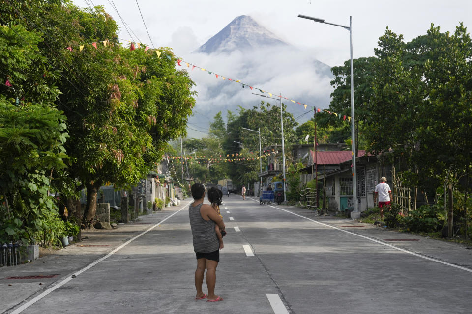 A woman and a girl look towards Mayon volcano in Legazpi, Albay province, northeastern Philippines, Tuesday, June 13, 2023. Truckloads of villagers on Tuesday fled from Philippine communities close to gently erupting Mayon volcano, traumatized by the sight of red-hot lava flowing down its crater and sporadic blasts of ash. (AP Photo/Aaron Favila)