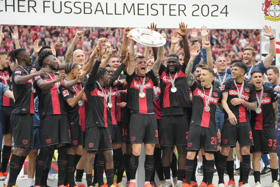Leverkusen's Granit Xhaka, centre, celebrates with the trophy as his team won the German Bundesliga, after the German Bundesliga soccer match between Bayer Leverkusen and FC Augsburg at the BayArena in Leverkusen, Germany, Saturday, May 18, 2024. Bayer Leverkusen have won the Bundesliga title for the first time. It is the first team in Bundesliga history, that won the championship unbeaten for the whole season. (AP Photo/Martin Meissner)