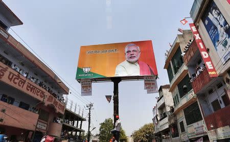 A supporter of Hindu nationalist Narendra Modi, prime ministerial candidate for BJP, holds onto a pole installed on a road divider showcasing a picture of Modi in Varanasi April 24, 2014. REUTERS/Adnan Abidi/Files