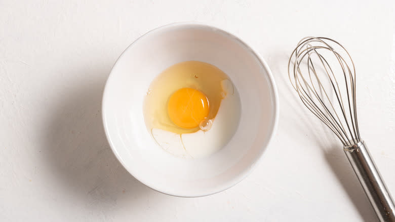Bowl with an egg and milk in it and a whisk on the side