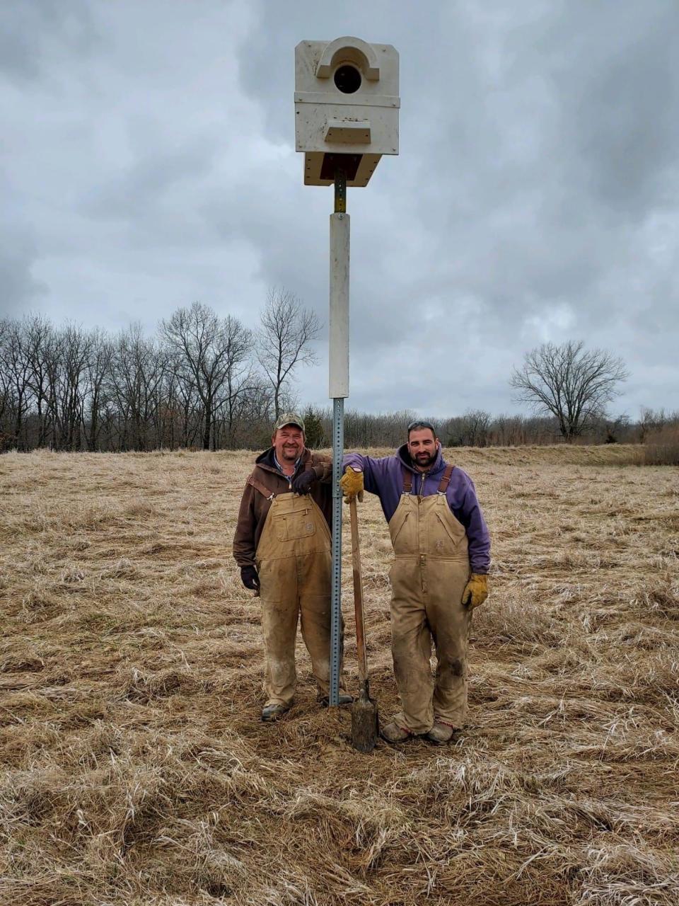 Two gentlemen stand next to a recently installed barn owl box, to help provide a safe place for the owls to raise their young and survive harsh weather conditions. Residents can build and install these boxes on their own land.