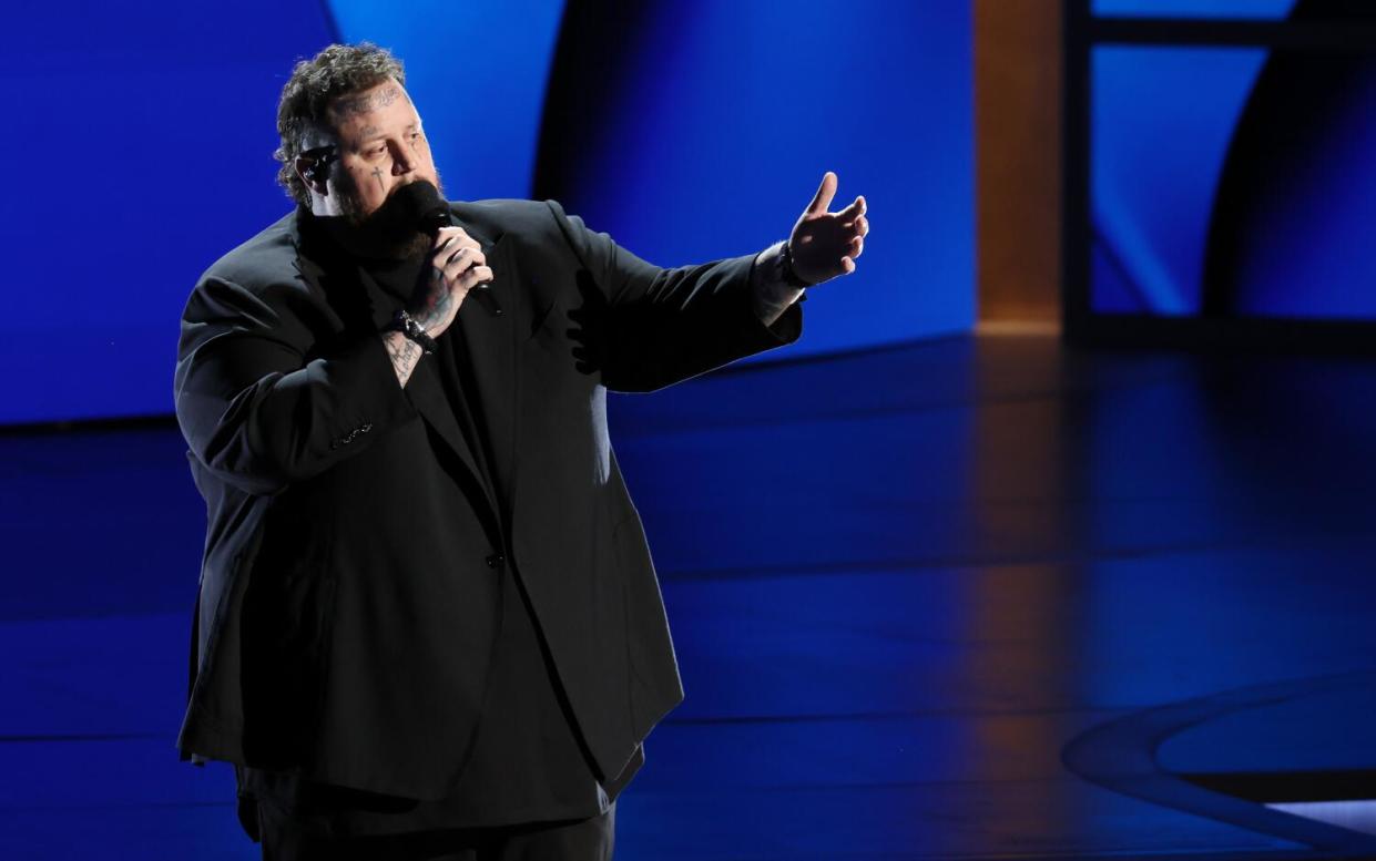 Jelly Roll onstage, singing into a microphone and gesturing with one hand