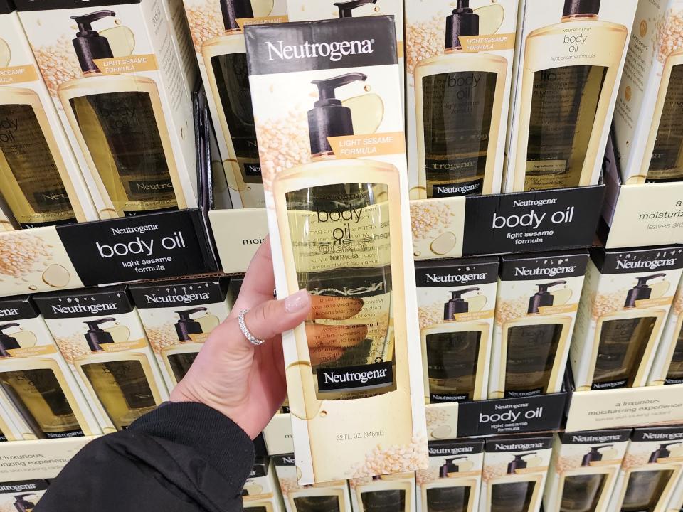 The writer holds a clear bottle of Neutrogena body oil in front of other boxes