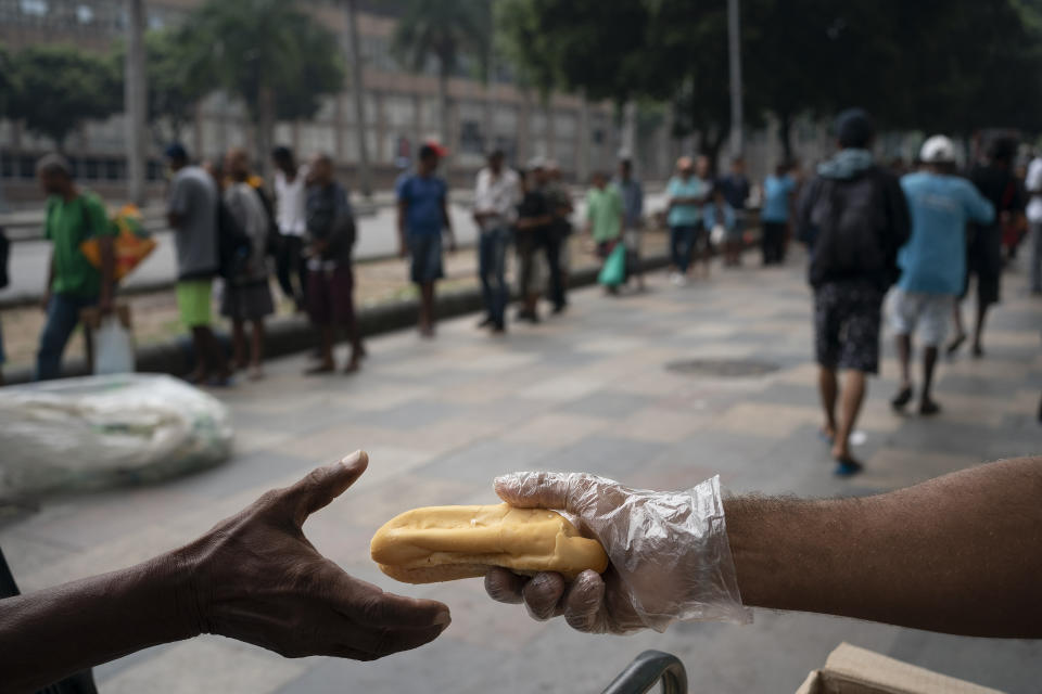 Homeless people gather for a free cup of coffee and bread from a private charity in downtown in Rio de Janeiro, Brazil, Monday, March 30, 2020, while most other residents are staying home to help contain the spread of the new coronavirus. (AP Photo/Leo Correa)