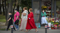 A flower vendor with a mask for protection against the COVID-19 infection partially covering her face watches people passing by in Bucharest, Romania, Friday, Sept. 18, 2020. (AP Photo/Andreea Alexandru)