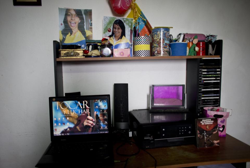 A laptop and pictures of Karen Palacios stand on her desk at her house in Los Teques in the outskirts of Caracas, Venezuela, Tuesday, July 16, 2019. Karen Palacios who plays the clarinet and was cut from the National Philharmonic for criticizing the government, and who was detained for 6 weeks, was released today. (AP Photo/Ariana Cubillos)