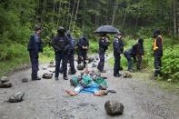 A woman plays a trumpet while lying on the road as RCMP officers assemble during an operation to arrest protesters in the Fairy Creek area of Vancouver Island