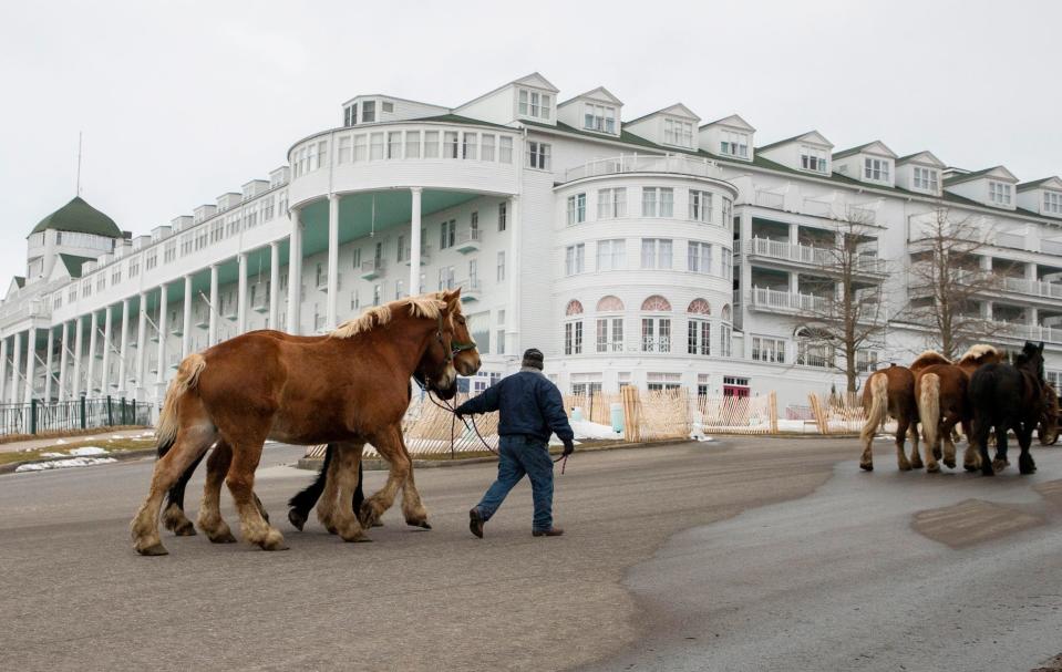Alex Bazihau, left, walks with three horses as he follows Jim Pettit to the stables located behind the Grand Hotel on Mackinac Island on Monday, April 4, 2022.