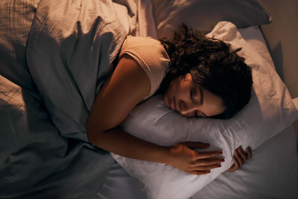 A person lies in bed, holding a pillow close while sleeping. Their hair is spread out on the pillow and their face is relaxed