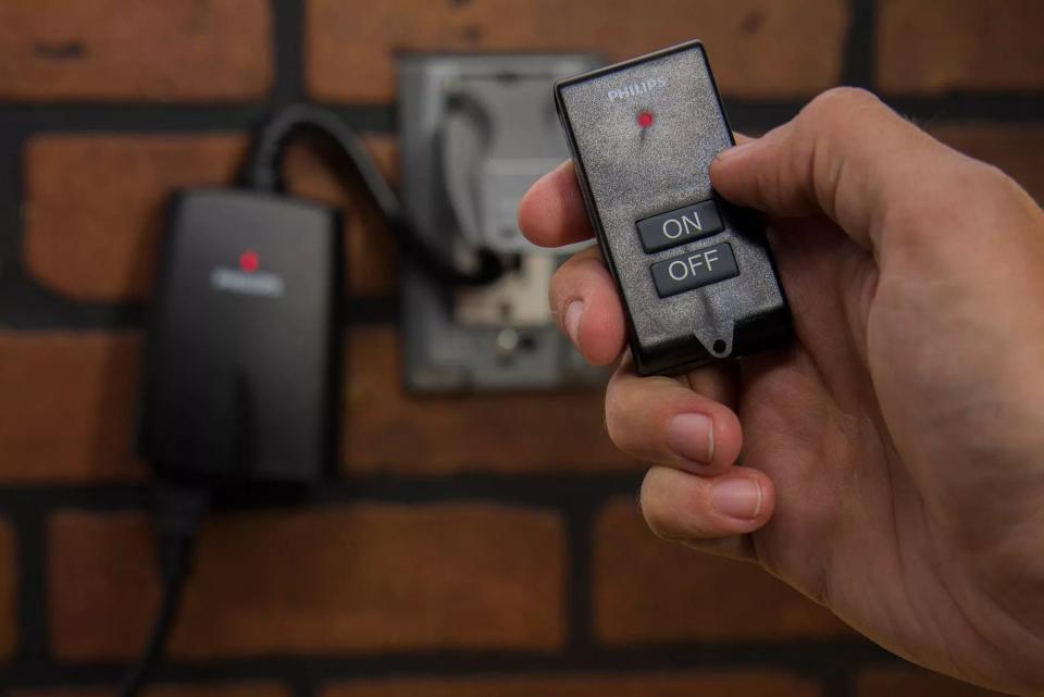 a hand holding the on/off remote control in front of the plug-in