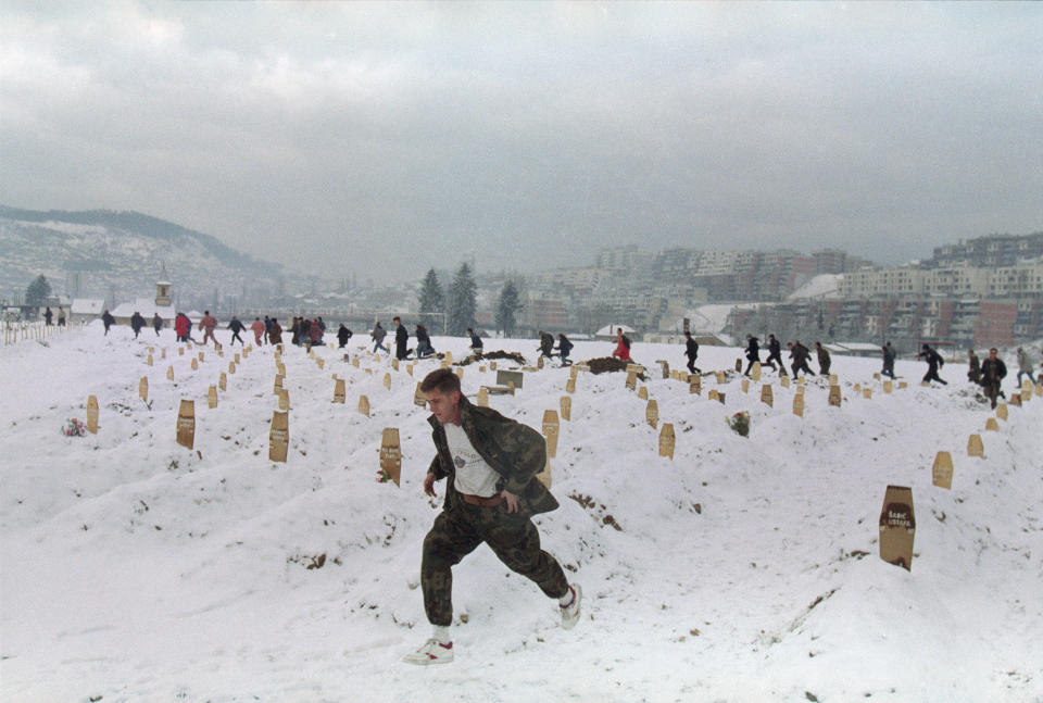 FILE - In this Feb. 20, 1993 file photo, a Bosnian soldier and other people in the background run for cover as Sarajevo's snow-covered military cemetery comes under a shell attack during a funeral for a soldier. Western countries are reeling from the coronavirus pandemic, awakening to a new reality of economic collapse, overwhelmed hospitals and home confinement. But for millions across the Middle East and in conflict zones elsewhere, much of this is familiar. (AP Photo/Hansi Krauss, File)