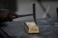 An employee uses a hammer to clean a gold ingot during the refining process at AGR (African Gold Refinery) in Entebbe